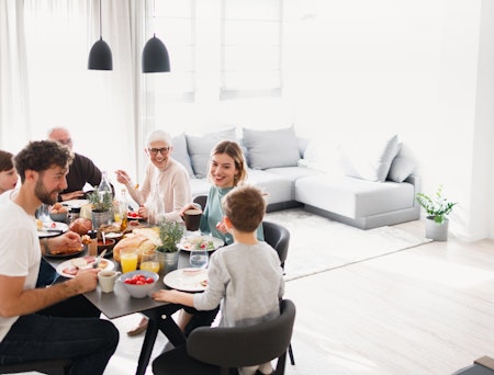 Seks smilende personer fra flere generasjoner er samlet rundt et bord og spiser.