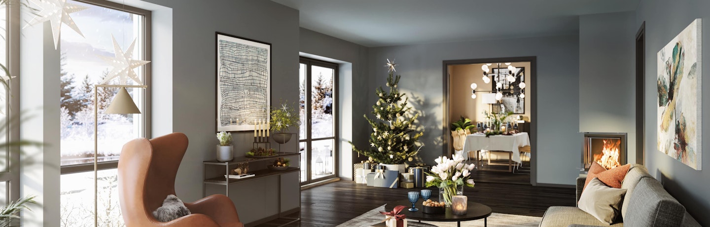 Julepyntet stue i ferdighuset Himin med gråblå vegger og innebygd peis. Hvite julestjerner i vinduet, juletre med pakker under i et hjørne og åpne dører inn til spisestue klar for julemiddagen.