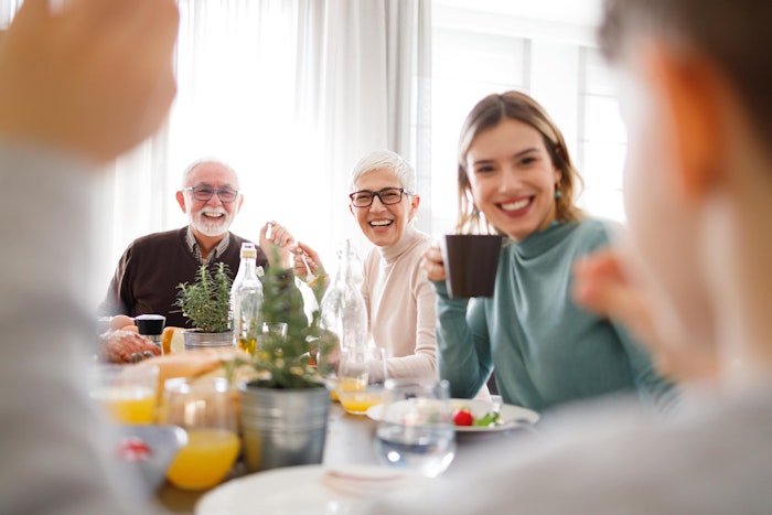 Nærbilde av smilende personer fra flere generasjoner som er samlet rundt et bord og spiser.