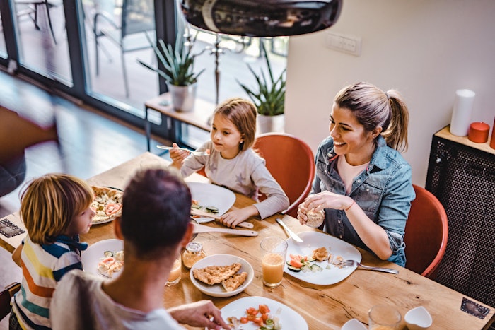 Kvinne og mann sitter med to barn og spiser ved et kjøkkenbord.