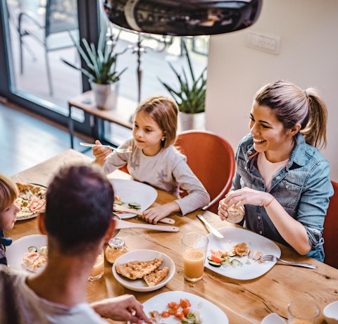 Kvinne og mann sitter med to barn og spiser ved et kjøkkenbord.