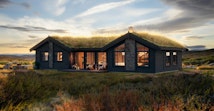 Himmelhø 1 er en praktfull hytte som her presenteres på en flat tomt i fjell-landskap. Det er kveldsstemning på illustrasjonen og det lyser varmt ut av vinduene i hytta. Det