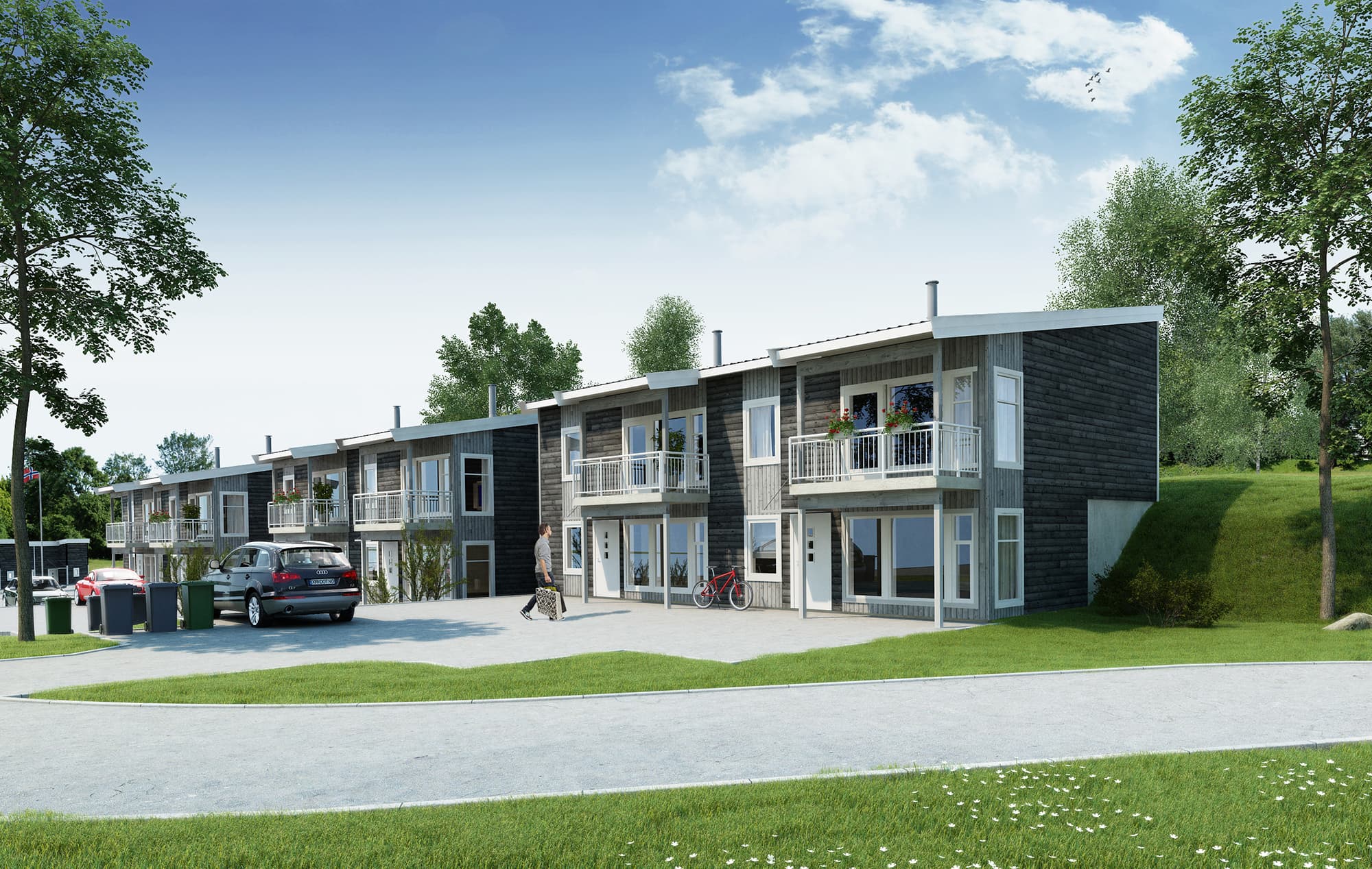 Miljøbilde av flere tomannsboliger av modellen Linde. Fra fellesområder med plen og parkeringsplass med en person gående mot en av boligene.