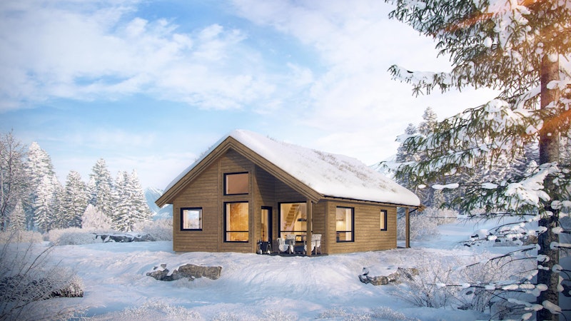 En brunbeiset liten hytte i vinterdrakt. Hyttemodellen Frikk har en overbygd liten veranda og et lite vindu på hemsen som slipper lyset inn til hemsen og gjør det koselig der oppe.