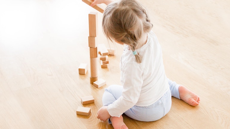 Bakhodet av en liten jente med musefletter som sitter på gulvet og bygger tårn av treklosser.